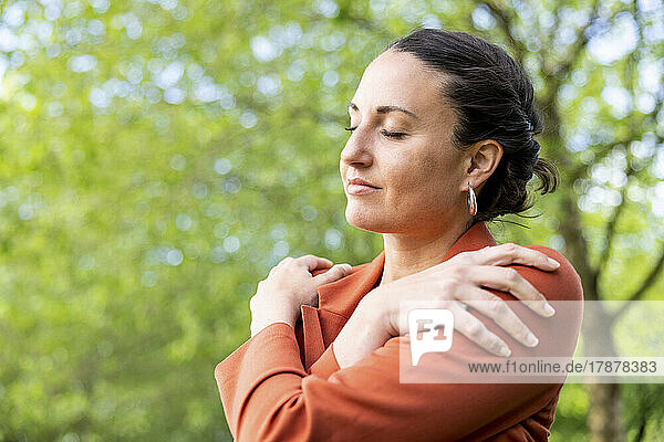 Businesswoman with eyes closed embracing herself in park