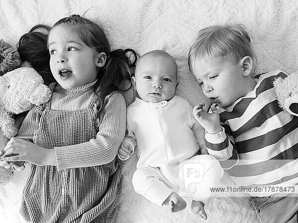 Brother and sister (2-3) with newborn boy (0-1 months) on bed