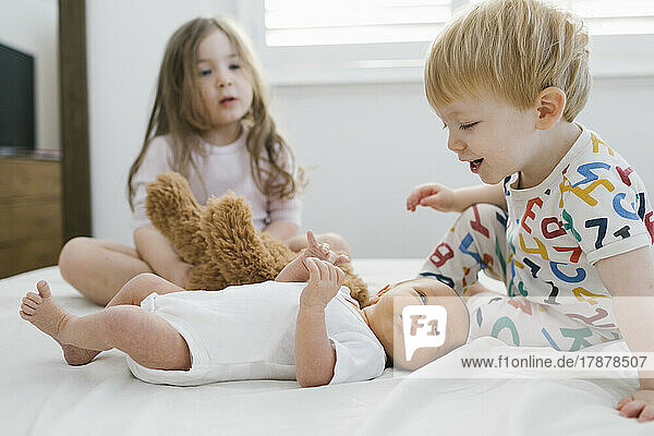 Brother and sister (2-3) with newborn boy (0-1 months) on bed