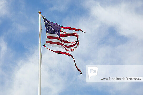 Torn American flag against sky