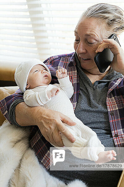 Grandmother holding newborn grandson (0-1 months) and talking on phone