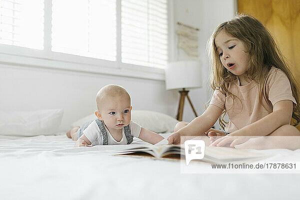 Girl (2-3) reading book to baby brother (6-11 months)