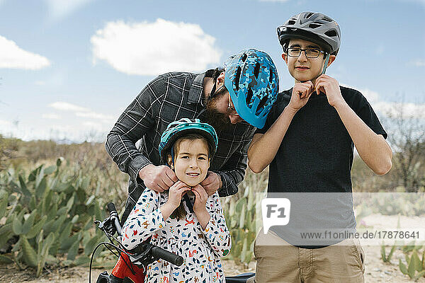Father and children (8-9  14-15) adjusting bike helmets