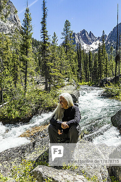 United States  Idaho  Stanley  Senior blonde woman hiking by rushing stream in mountains near Sun Valley