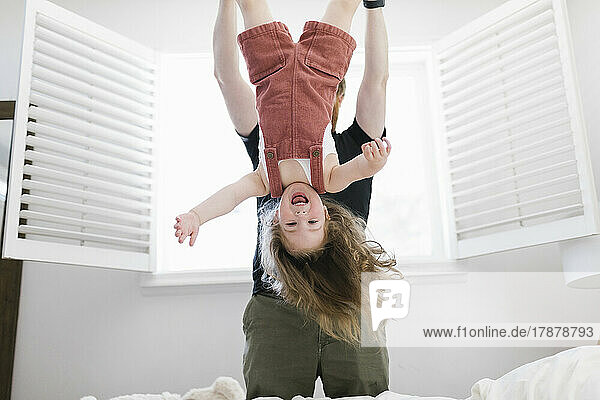 Father swinging daughter (2-3) playfully in bedroom