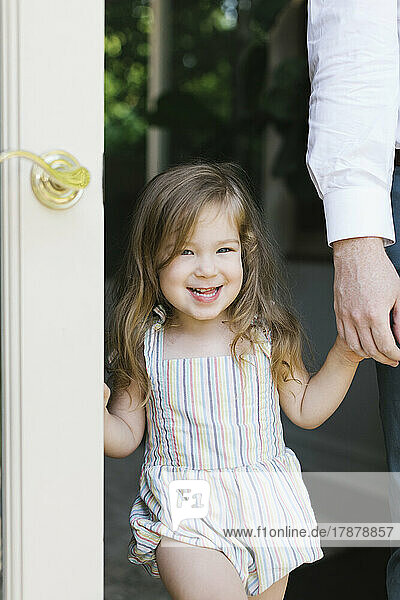 Portrait of smiling girl (2-3) holding fathers hand in doorway at home
