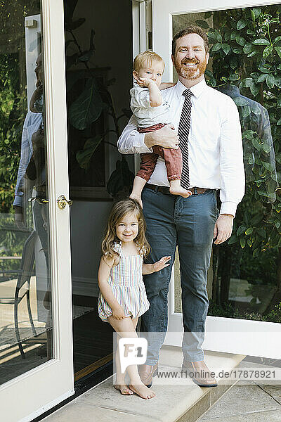Portrait of smiling father with son (12-17 months) and daughter (2-3) in doorway at home