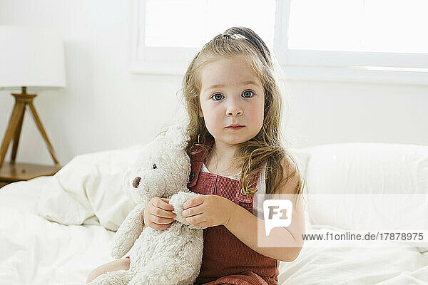 Portrait of girl (2-3) sitting on bed with teddy bear