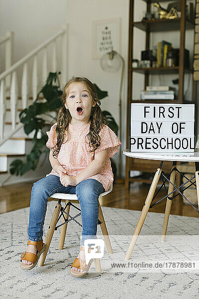 Portrait of girl (2-3) making faces at First day of preschool sign
