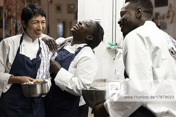 Multiracial chefs laughing while working in kitchen of restaurant