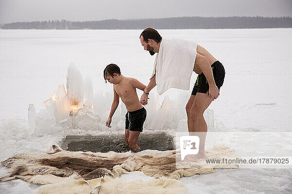 Mann hält die Hand seines Sohnes beim Eisbaden auf einem zugefrorenen See in voller Länge