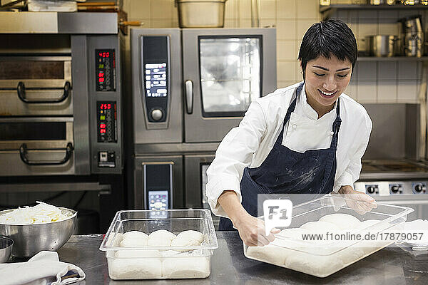 Lächelnder Koch  der ein Tablett aufhebt  während er in der Küche eines Restaurants arbeitet