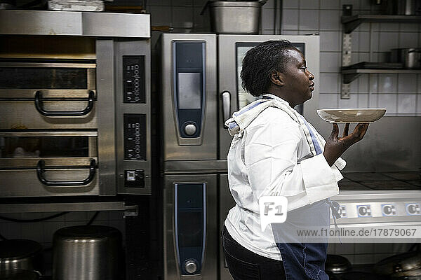 Side view of chef carrying plate while walking in commercial kitchen
