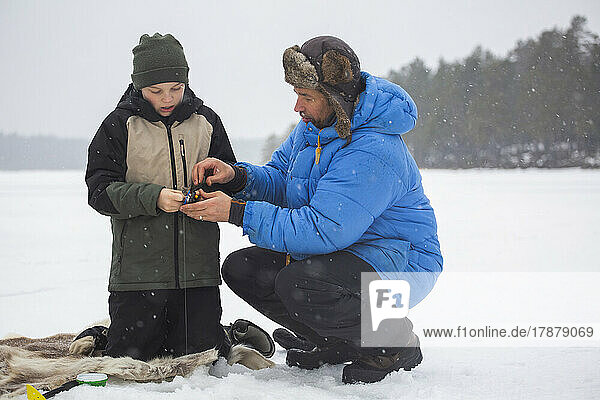 Mature man in warm clothing ice fishing with son on frozen lake