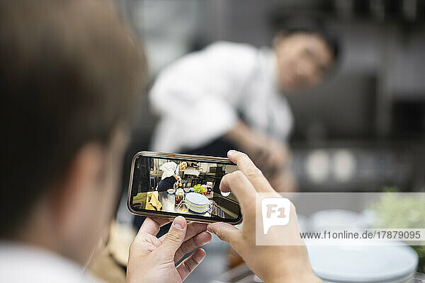 Chef photographing colleague preparing food in restaurant