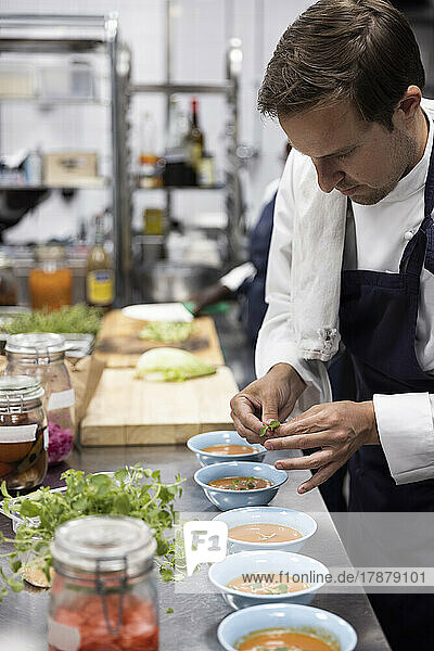 Koch garniert Suppe mit Basilikumblättern am Küchentisch im Restaurant