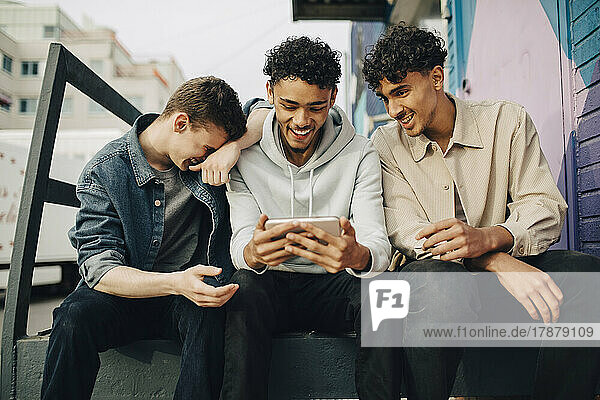 Happy man using smart phone while sitting with friends outdoors