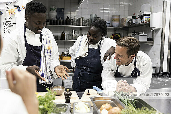 Chefkoch erklärt lächelnden multirassischen Kollegen in der Küche eines Restaurants