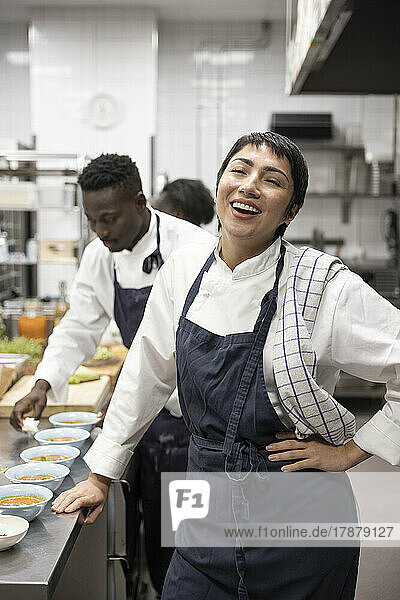 Porträt eines lachenden Kochs  während ein Kollege in einer Restaurantküche Schüsseln abwischt