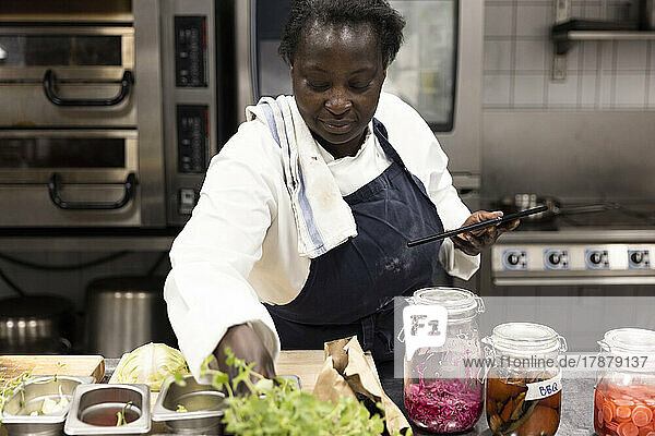 Chefkoch hält digitales Tablet bei der Zubereitung von Speisen in der Küche eines Restaurants