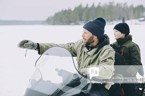 Reifer Mann gestikuliert beim Schneemobilfahren mit Jungen