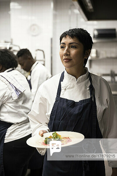 Weibliche Köchin trägt Teller mit Essen  während sie in der Küche eines Restaurants geht