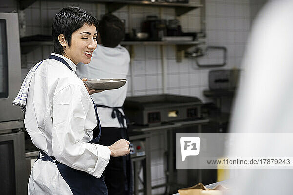 Smiling female chef carrying plate walking in commercial kitchen
