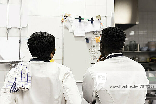 Rückansicht von multirassischen Köchen  die in der Küche eines Restaurants ein Brainstorming über einem Whiteboard durchführen