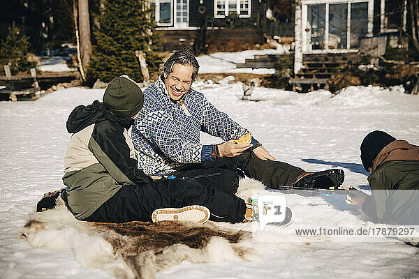 Lächelnder Vater im Gespräch mit seinem Sohn beim Angeln im Schnee liegend an einem sonnigen Tag