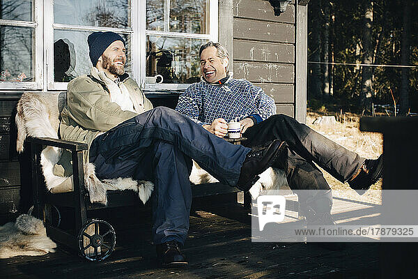 Fröhliche reife Männer unterhalten sich beim gemeinsamen Kaffee auf der Veranda im Winter