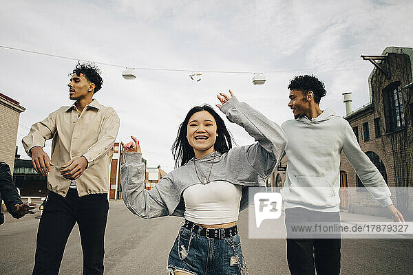 Happy multiracial young woman dancing with friends on street in city