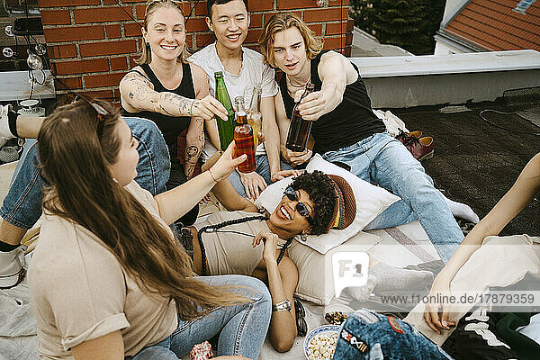 Happy male and female toasting beer bottles enjoying on rooftop