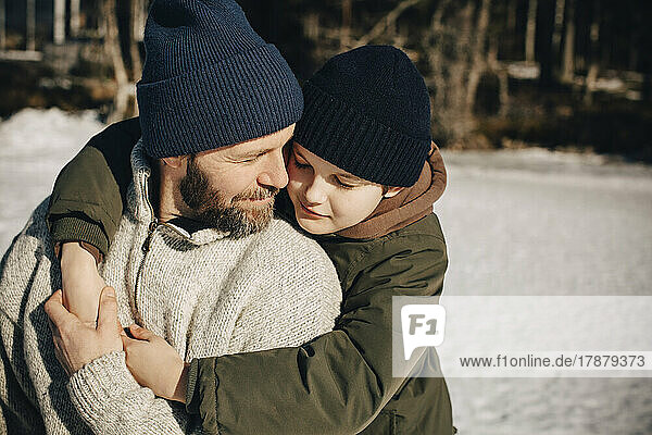 Zärtlicher Vater und Sohn mit Strickmütze umarmen sich an einem sonnigen Tag