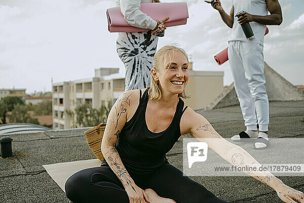 Glückliche Frau  die Yoga praktiziert  während Freunde auf dem Dach stehend miteinander reden