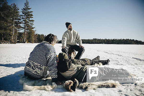 Father and son sitting on animal skin while ice fishing with friends enjoying sunny day in winter