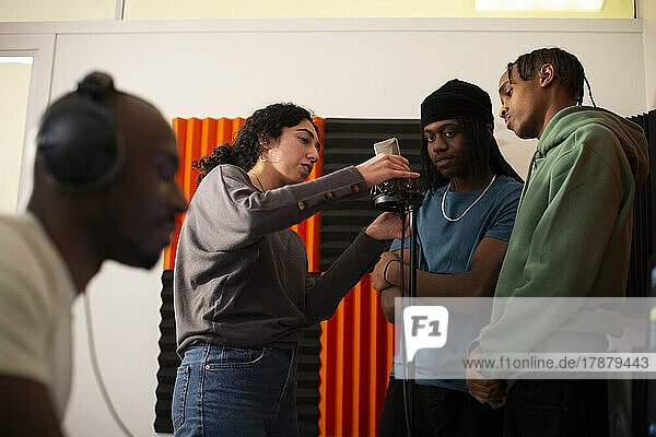 Woman adjusting microphone while rappers standing in studio
