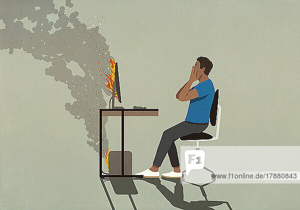 Shocked man sitting at smoking computer on fire