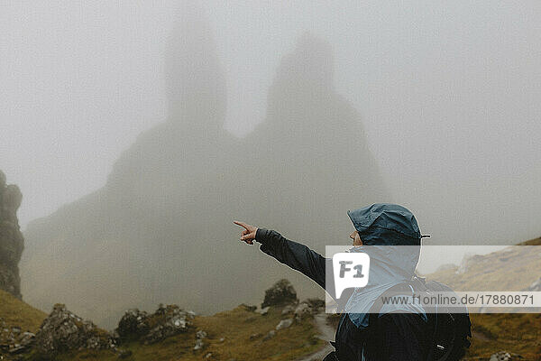 Man in ran jacket hiking below foggy Old Man of Storr rock formation  Scotland