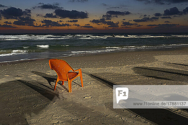 Orange lawn chair on sandy beach at dusk  Bat Yam  Israel