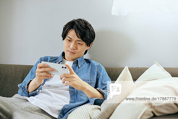 Japanischer Mann benutzt Smartphone auf dem Sofa