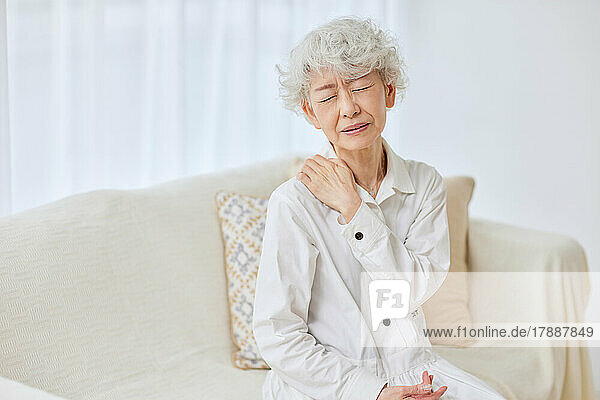 Japanische Seniorin mit Schmerzen auf dem Sofa