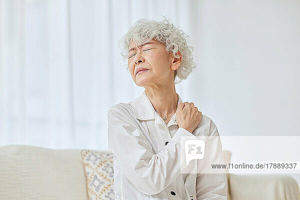 Japanische Seniorin mit Schmerzen auf dem Sofa