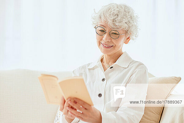 Japanese senior woman reading a book on the sofa