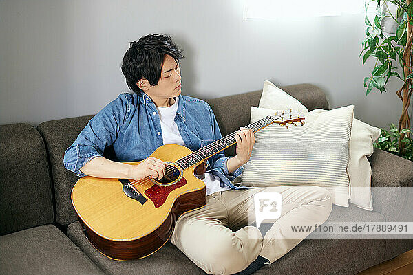Japanischer Mann spielt Gitarre auf dem Sofa