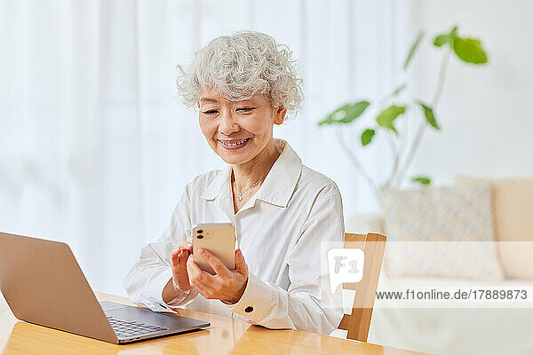 Japanische Seniorin benutzt Laptop und Smartphone zu Hause