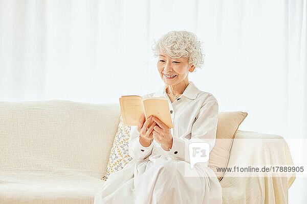 Japanese senior woman reading a book on the sofa