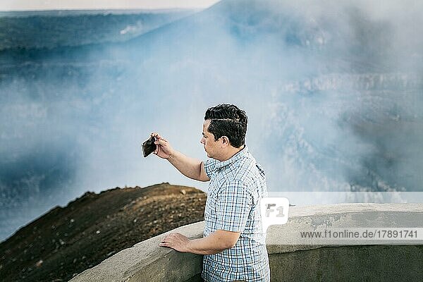 Tourist  der an einem Aussichtspunkt Fotos macht. Junger Tourist  der an einem vulkanischen Aussichtspunkt Fotos macht. Abenteuerlustiger Mann mit seinem Mobiltelefon  der an einem Aussichtspunkt Fotos macht. Volcán Masaya  Nicaragua  Mittelamerika
