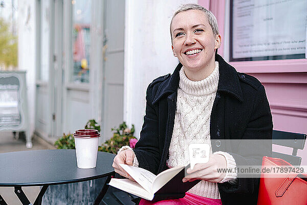 Happy woman reading book at sidewalk cafe