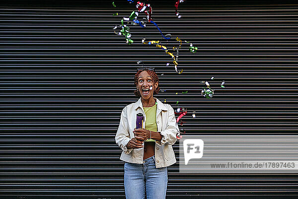 Playful woman with party popper in front of wall