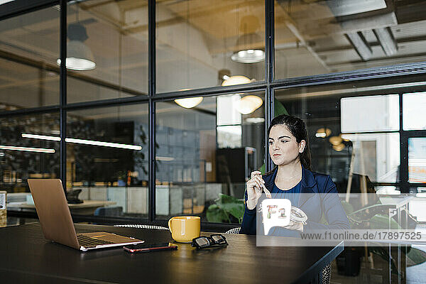 Young businesswoman having fruits and watching laptop in office